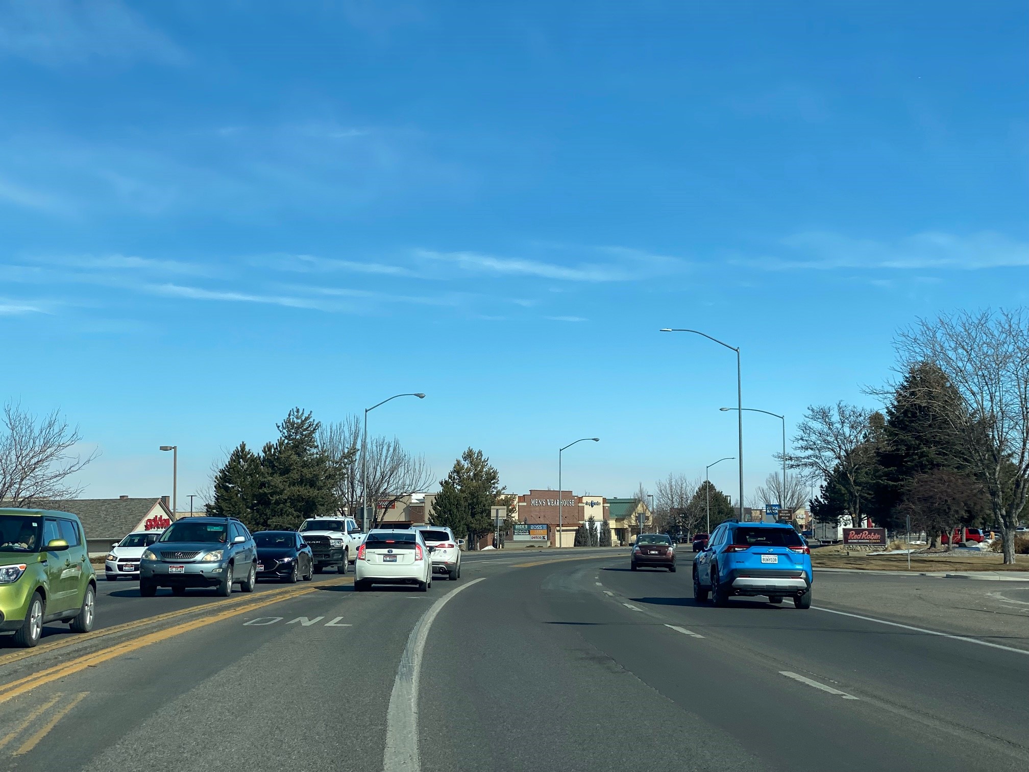 Image of a stretch of Blue Lakes Boulevard with vehicles, clear sky, trees, structures, and street lights.